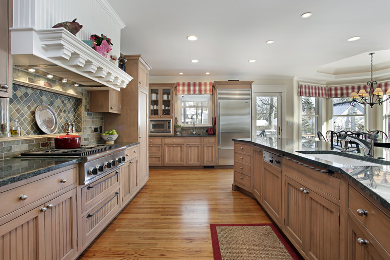 Large craftsman style custom kitchen with light wood cabinets. gas stove, slate backsplash and dark countertops
