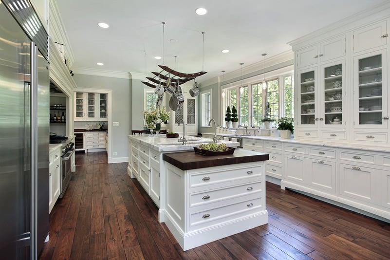 Luxury white kitchen with marble island, hanging pots and pans and hardwood flooring