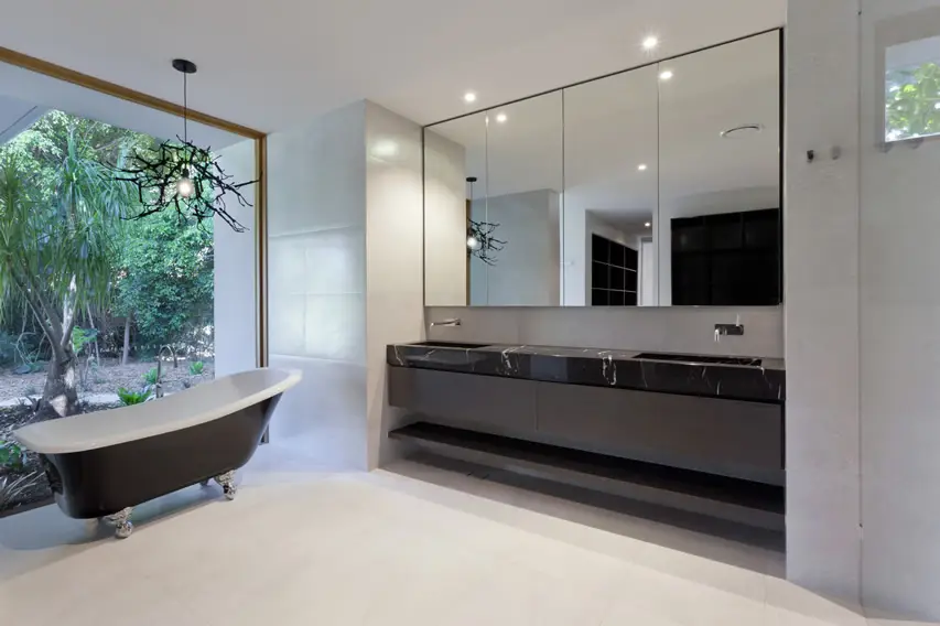 White bathroom with black pedestal tub, frameless mirror and panoramic window