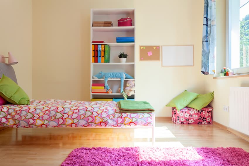 Room with yellow painted walls, open shelf, pink rug and green pillows