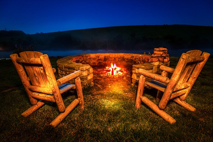 C-shaped rock fire pit with rustic wood chairs