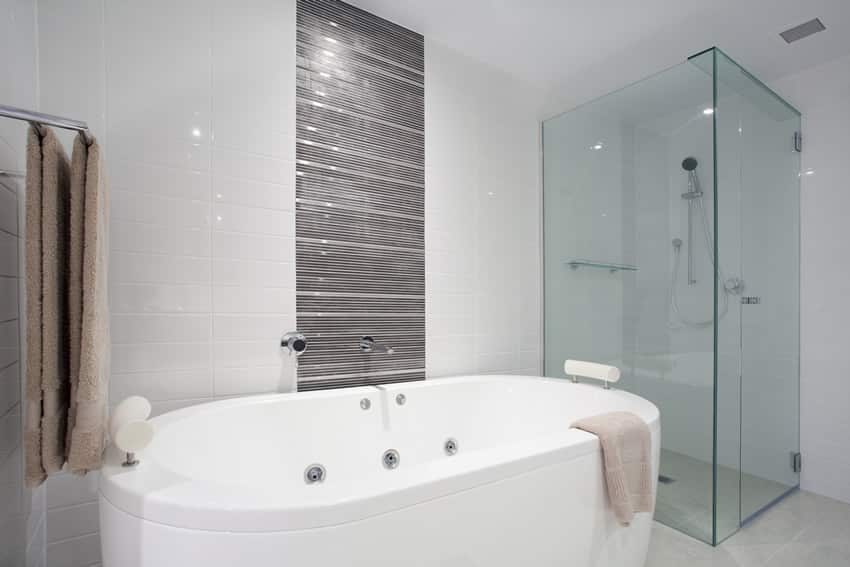 Bathroom with shower area with tempered glass, white tub and towel rack