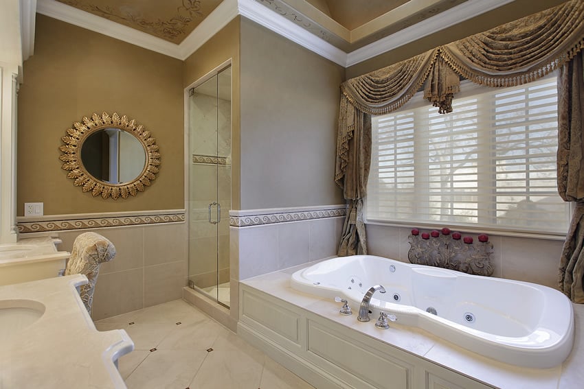 Cream-colored bathroom with round mirror tub and window with brocade drapery