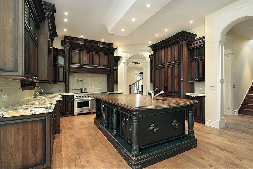 Kitchen with walnut cabinets, light granite counters, white arches and butcher block island