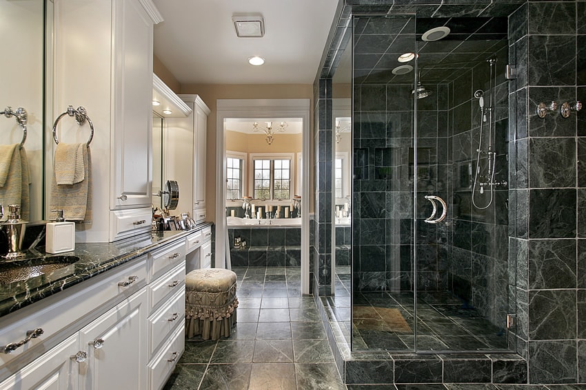 Bathroom with dark marble vanity counters and shower space with natural stone tiles