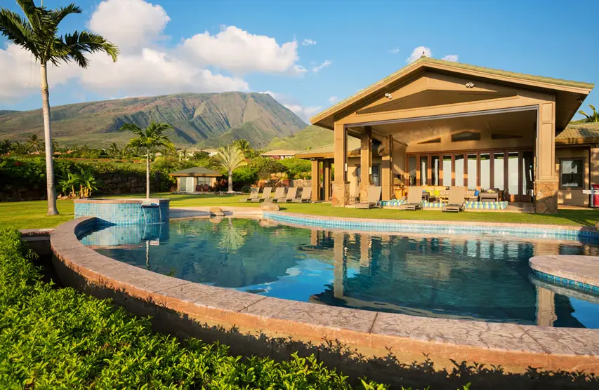 Pool in bean shape with blue tiles and surrounded by grassy lawn