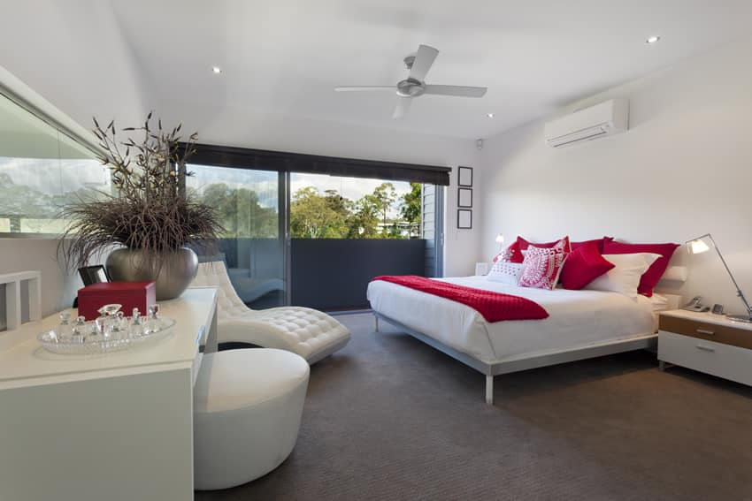 Bedroom with white lounge chair, red pillows and white ceiling fan