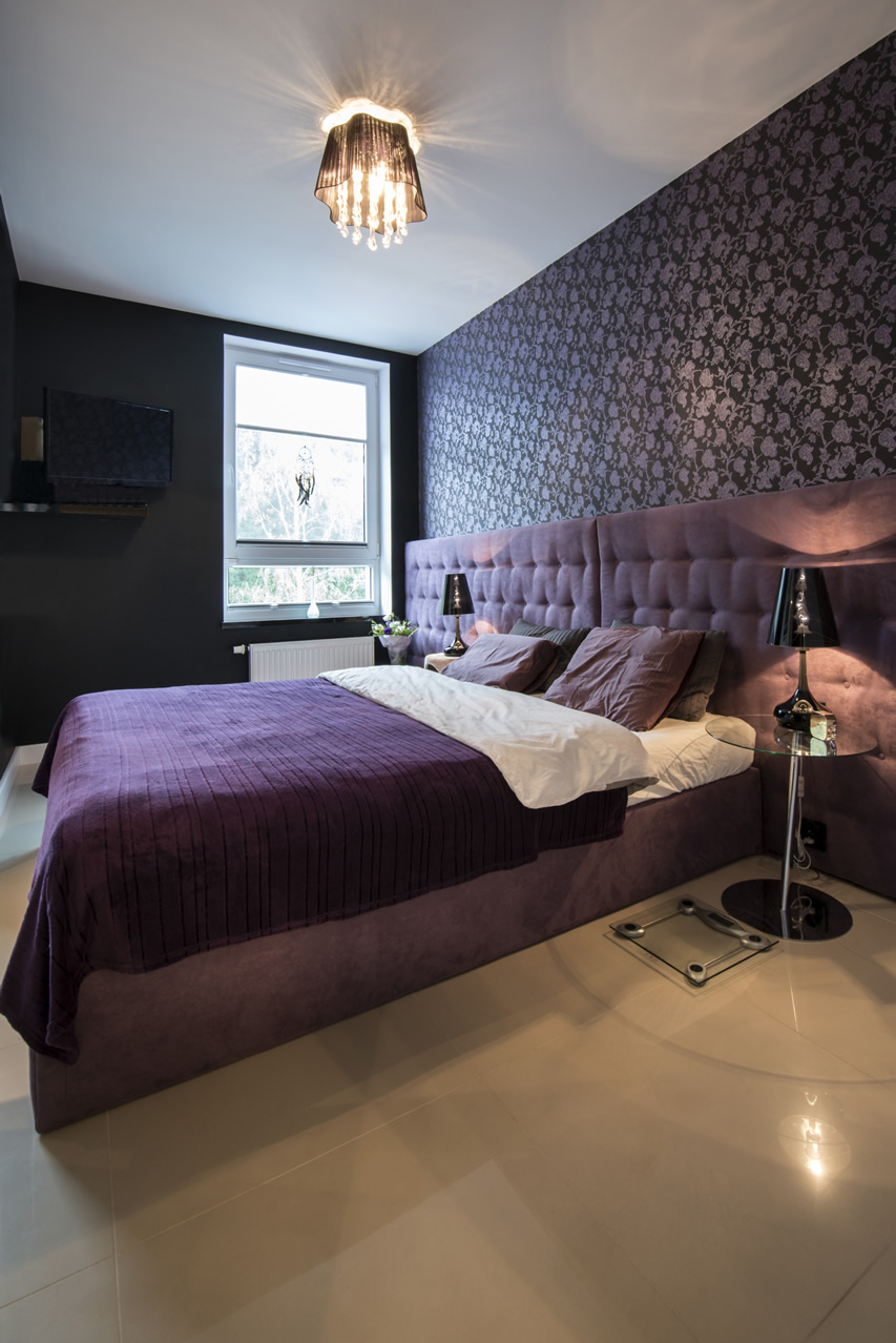 Room with wallpaper with purple floral pattern and bed with velvet headboard