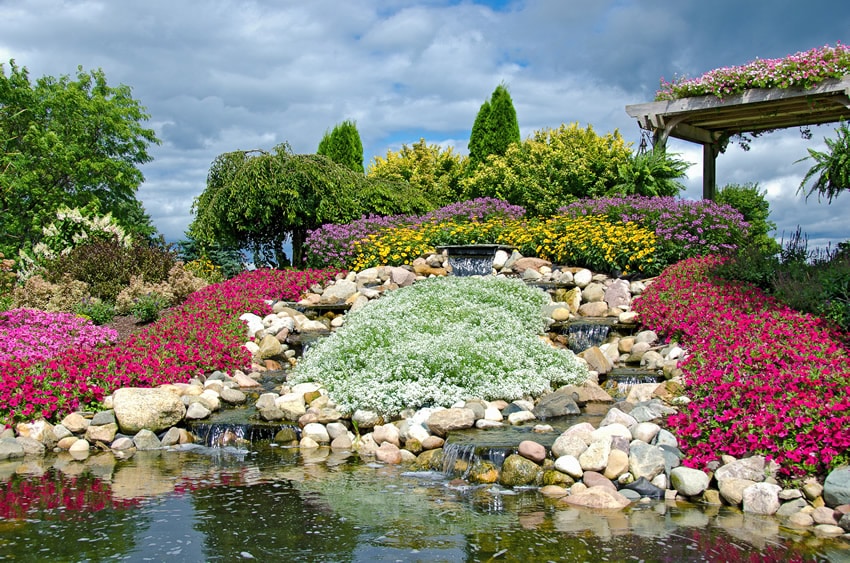 Rock stacked hill waterfall with colorful flowers and pergola