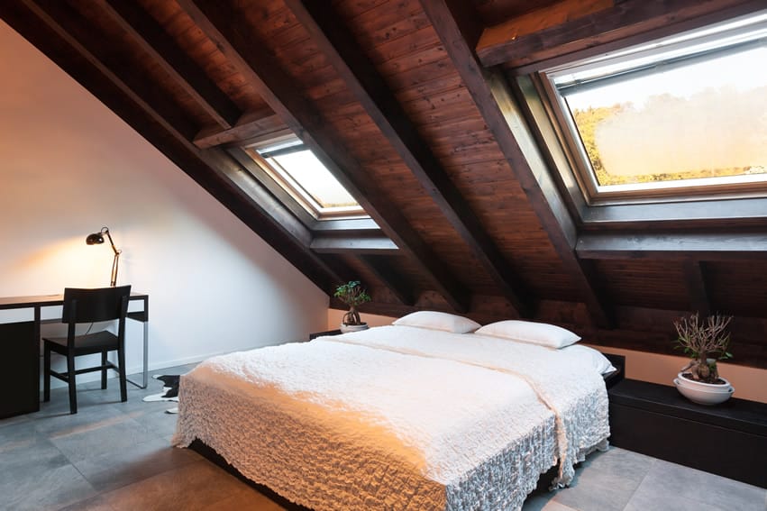 Room with gray stone tiles, exposed wooden ceiling slats and bed