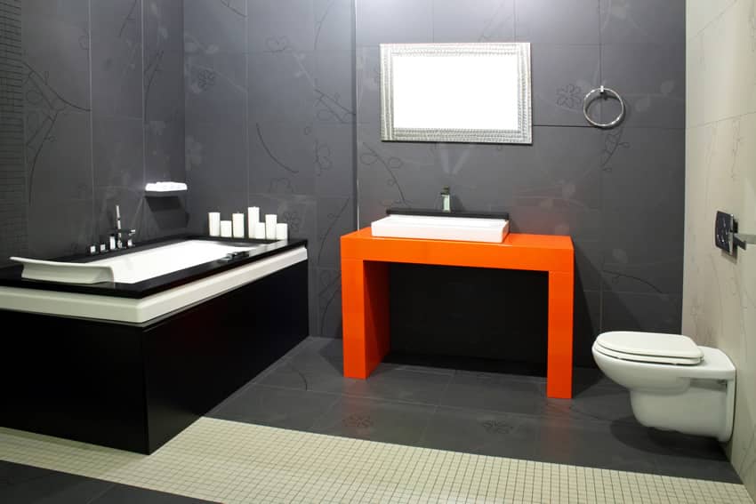 Bathroom with grey tiles behind water closet and bright orange vanity with ceramic wash basin