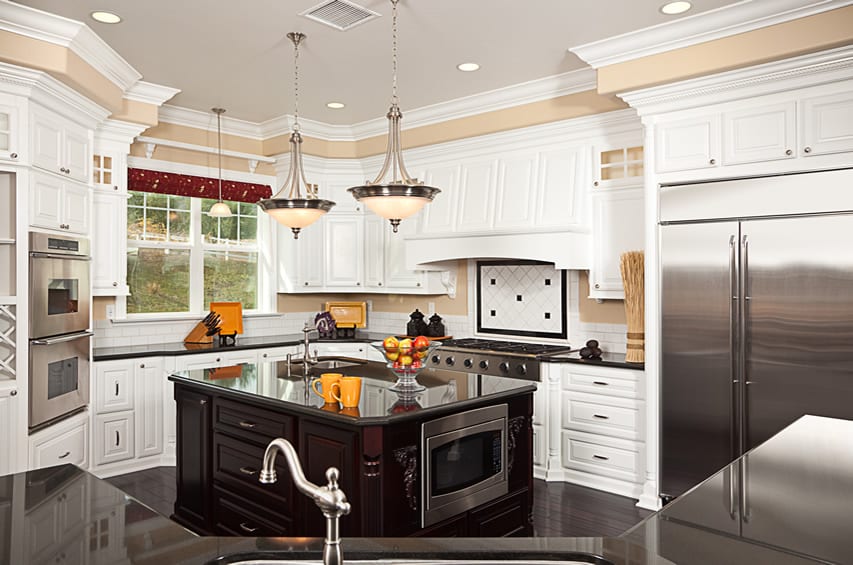 Custom country kitchen with white cabinets, black countertops, tile backsplash and island with sink