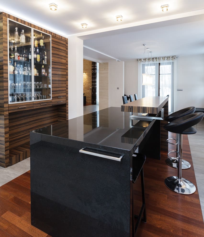 Bar area inside home with black quartz countertops and black leather and chrome barstools