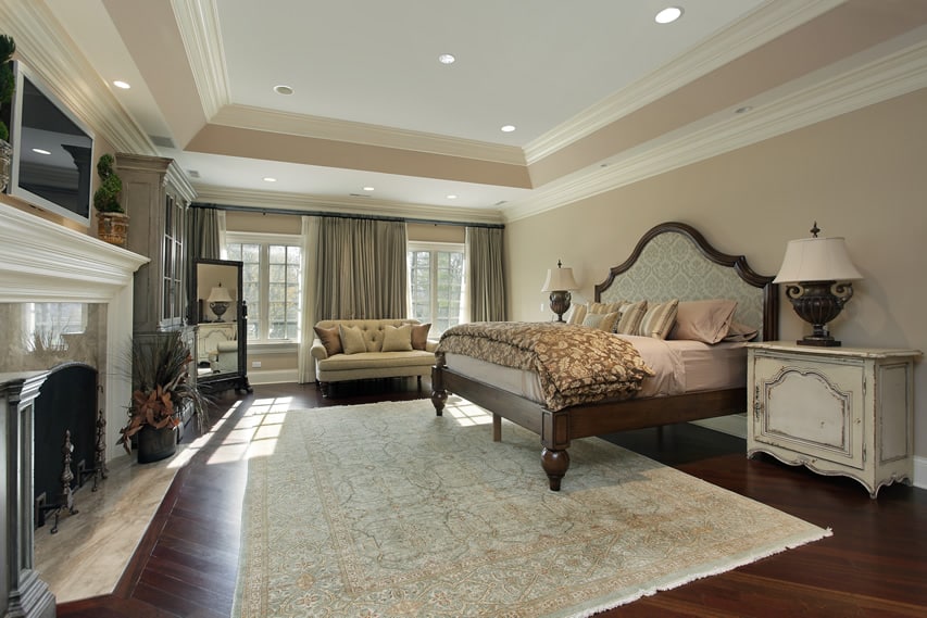 Bedroom with tray ceiling with fireplace and hardwood flooring