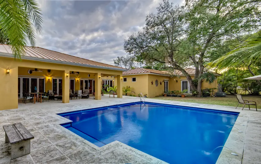 Pool with wide granite tiles behind a Mediterranean inspired home