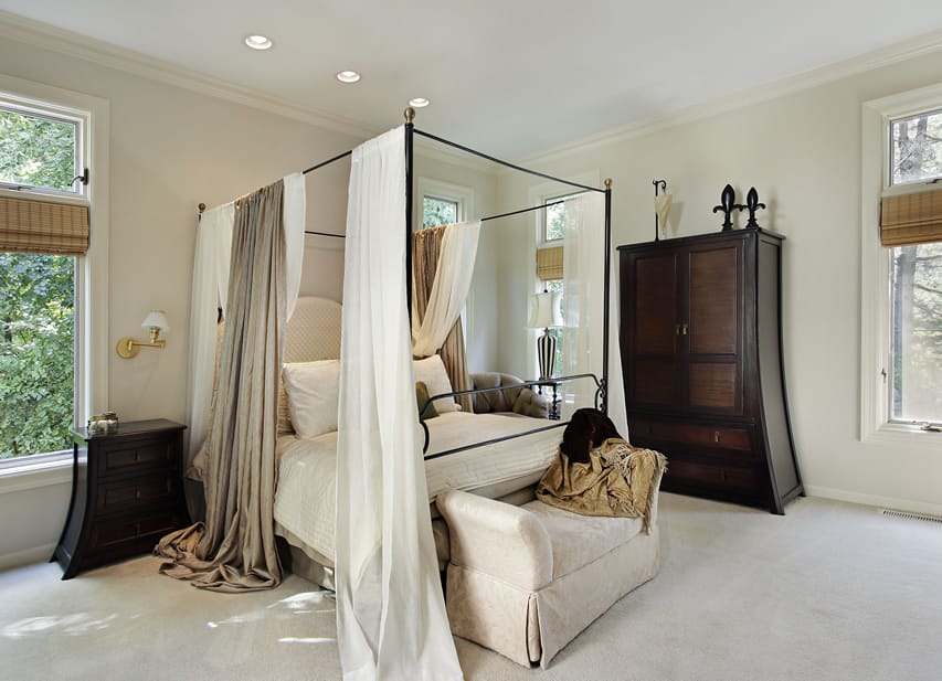 Beautiful four post bedroom with white curtains and interesting furniture pieces