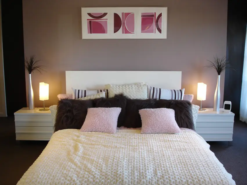 Wall with purple undertones, pink and brown pillows and metal vases 