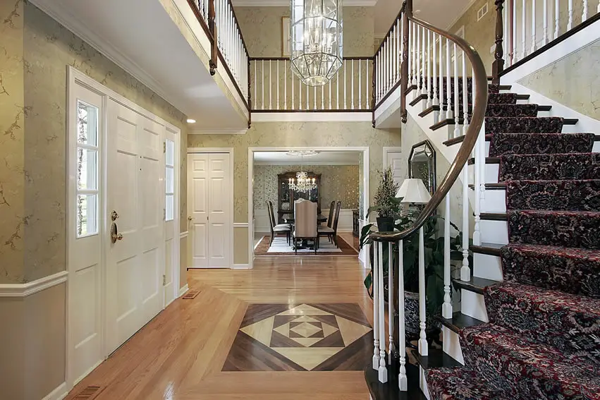 Foyer with parquet floors, white entry door and staircase with red carpet