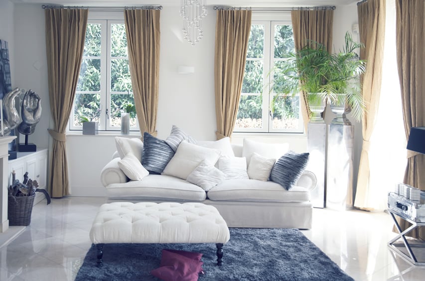 Living room with blue area rug, white couch and curtained windows