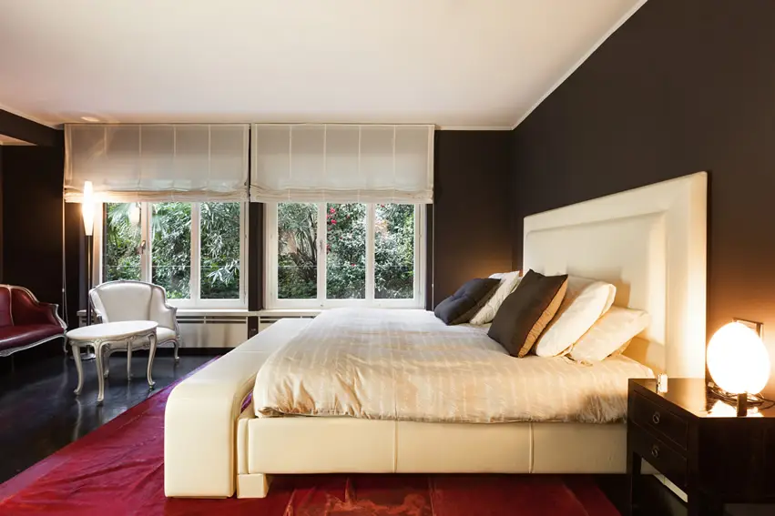Dark mocha walls, cream colored bed and red area rug