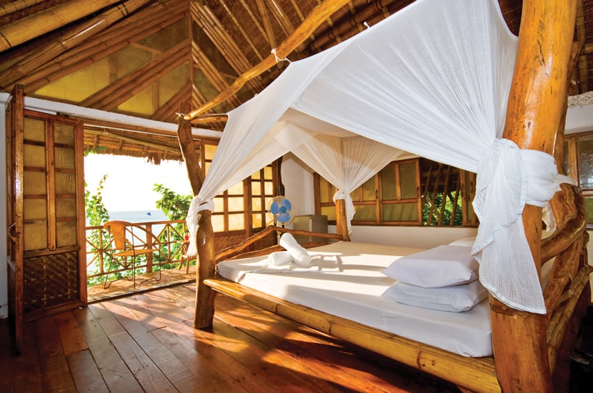 Bamboo and wood bed with white covers and overlooking an ocean