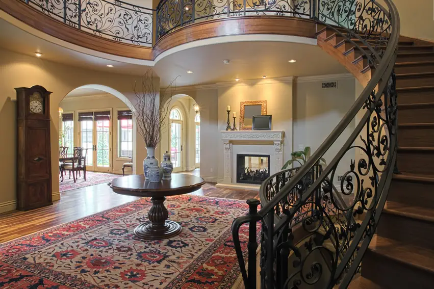 Foyer with round pedestal table with three jars on top, a grandfather clock and red carpet