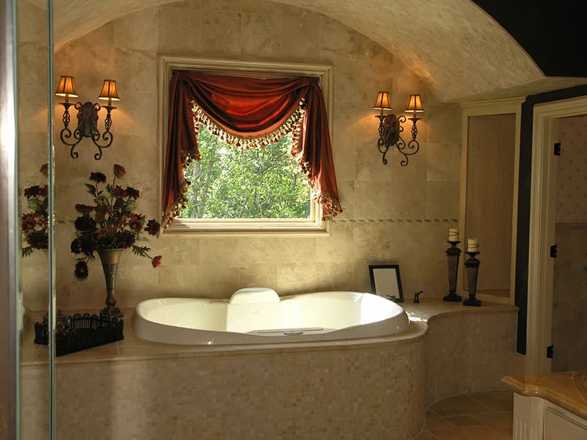 Elevated bathtub with two wall lamps and red window drapery