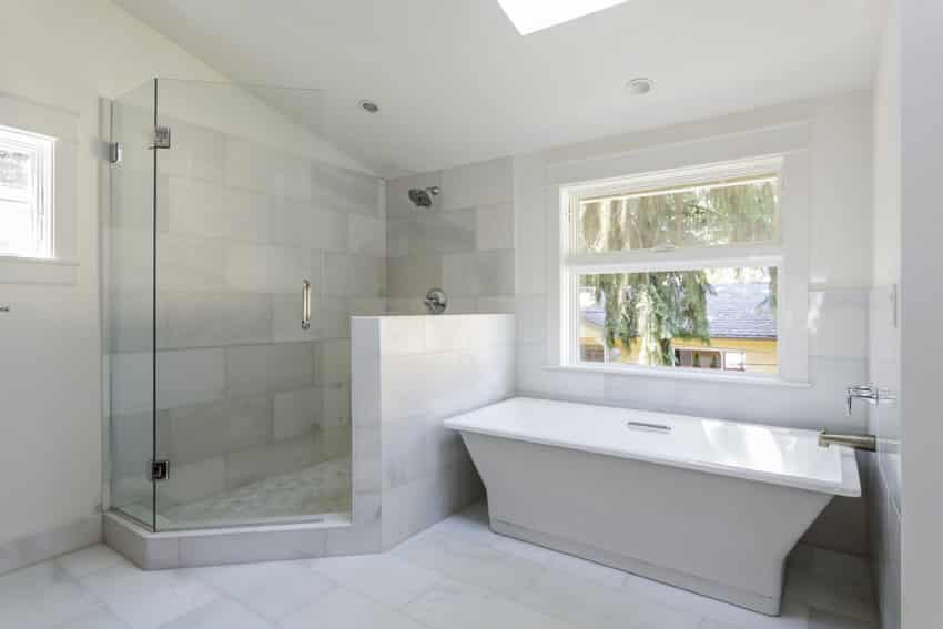 Bathroom with angular tub beside a shower with half glass and white tiled wall