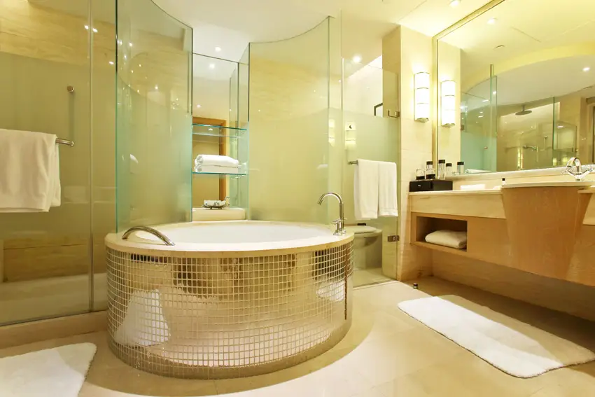 Circular bathtub with mirrored tile body and separate shower and toilet areas