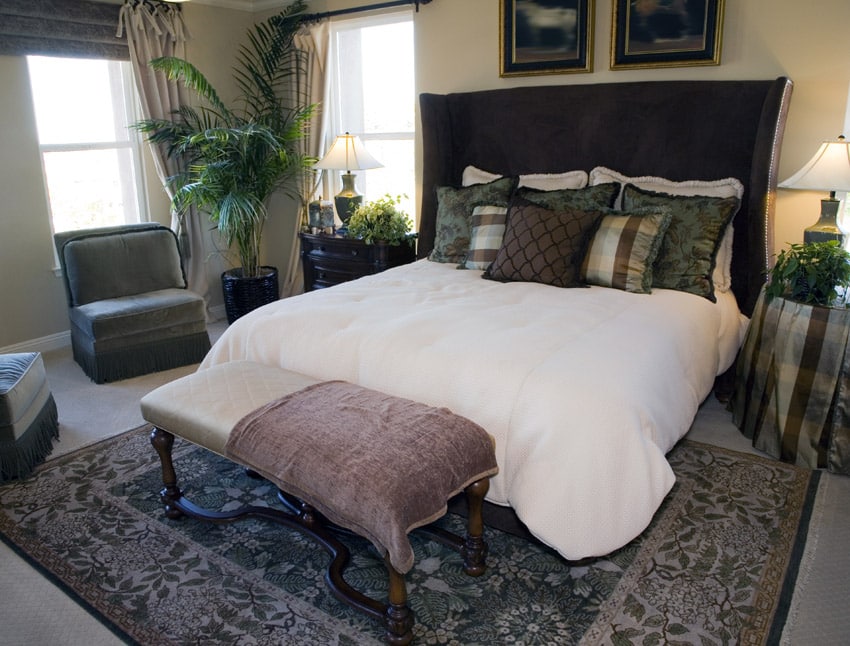 Bed with traditional print rug, green throw pillows and potted palm