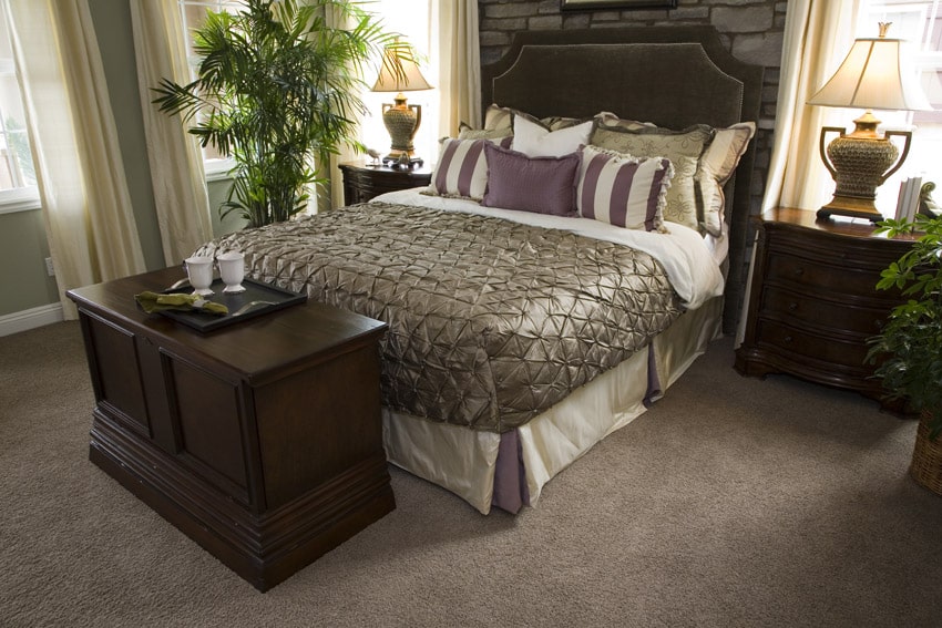 Bed with purple accents, tan carpet and walnut wood bedside tables