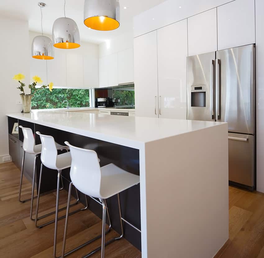 Kitchen with laminated counter with charcoal colored cabinets and white bar chairs