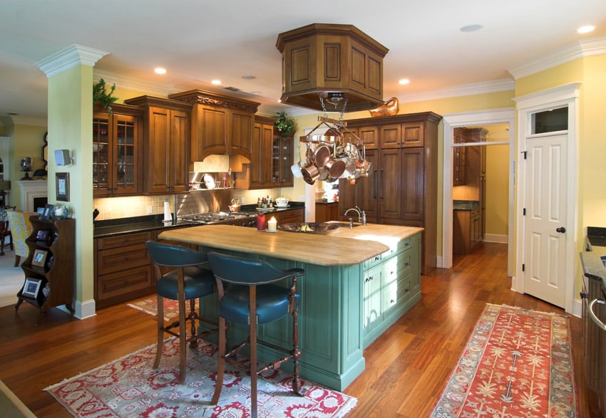 Semi open kitchen space with two-level island with teal base, carpets and leather stools