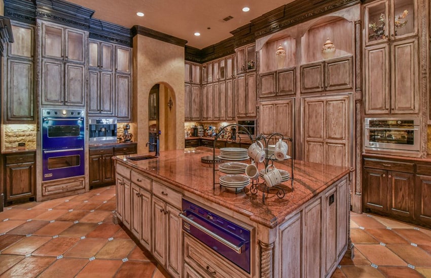 Wide rectangular island topped with red brown stone and diagonal tiles on the floor