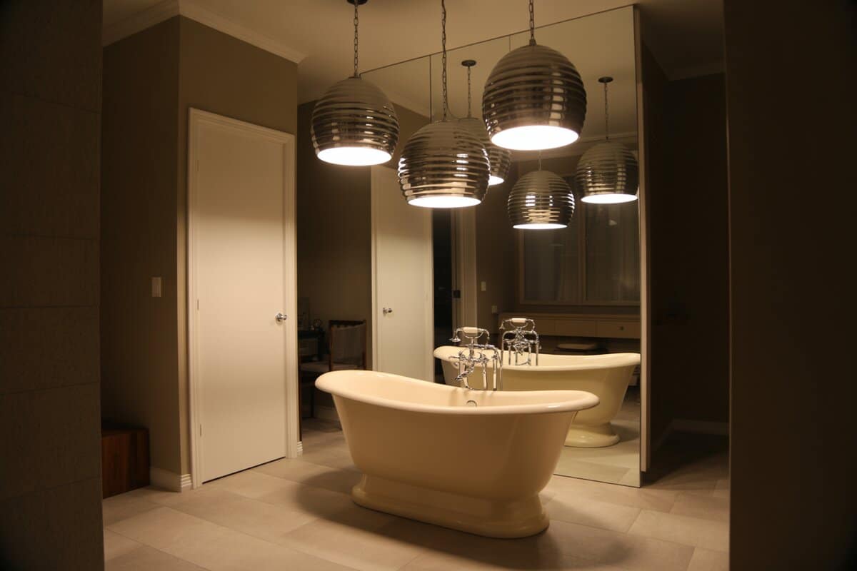 Four nickel beehive pendants suspended above a cream pedestal soaking tub