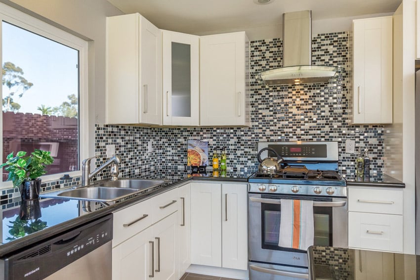 Compact kitchen with glass mosaic tile wall backsplash, white cabinets, dark counters