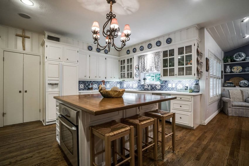 White cabinet kitchen with glass doors, collectible plates and butcher block island