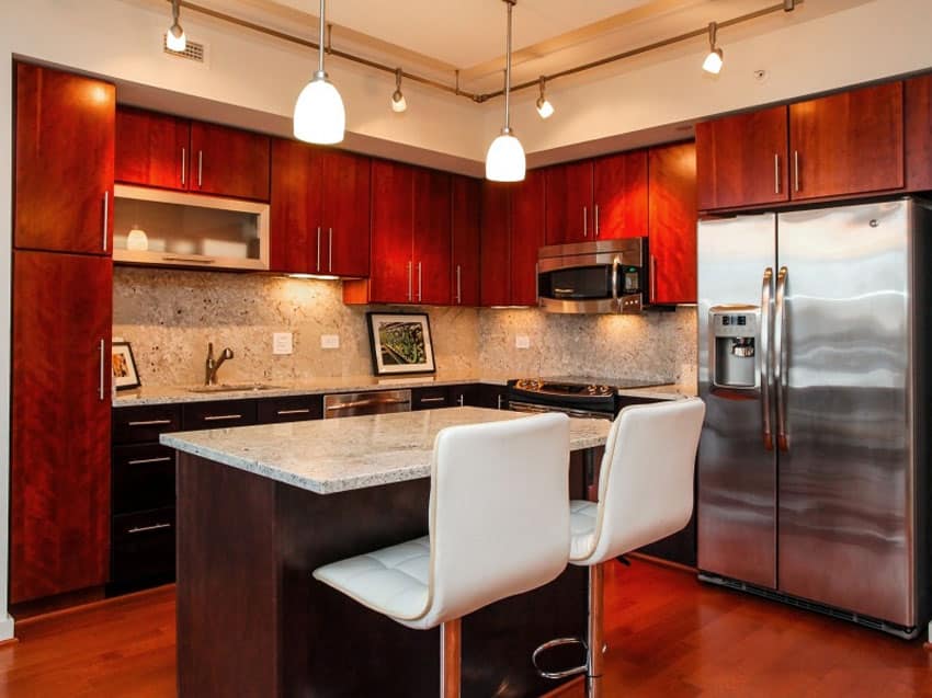 Kitchen with white island chairs, track lights and natural stone backsplash