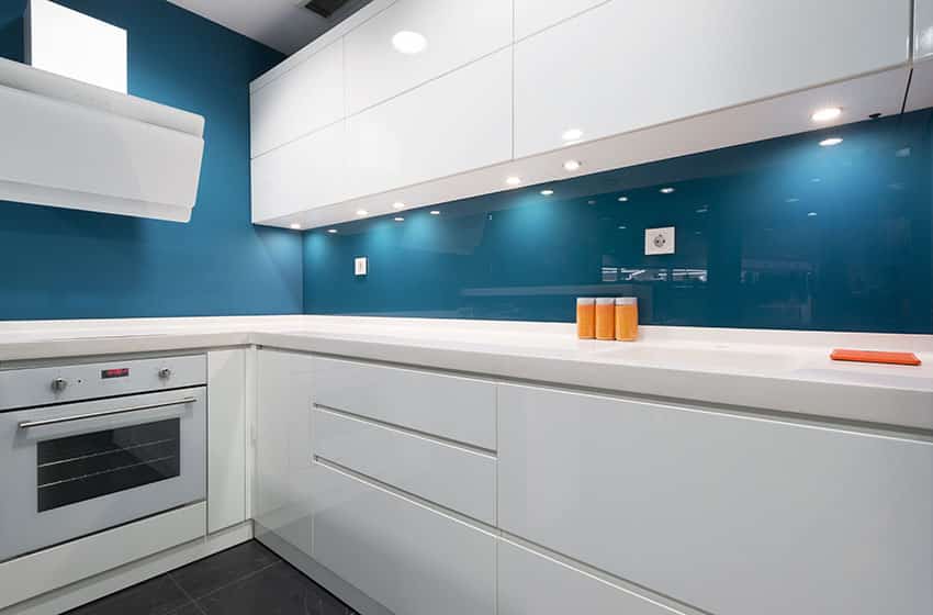 Modern l shaped kitchen with white cabinets white counters and blue glass backsplash