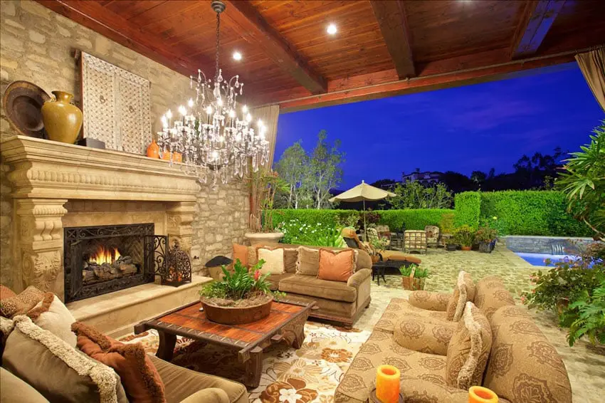 Outdoor fireplace at covered patio with chandelier and swimming pool view
