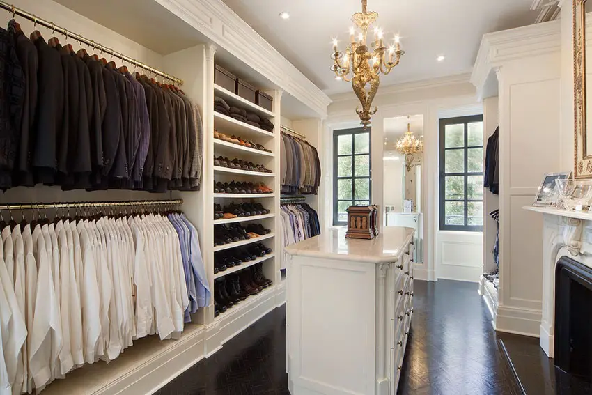Closet with dark wengue floors, ciothes organizd by color, wall mirror and candle type chandelier