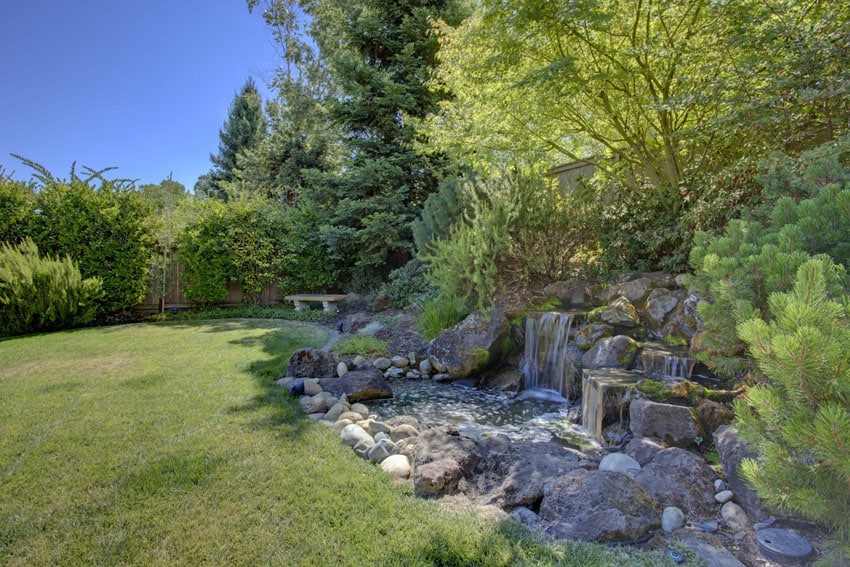 Stone waterfall and pond next to backyard lawn