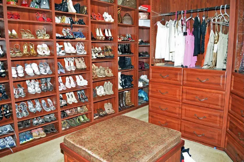 Closet with rack full of shoes on one side, an ottoman and shelves with drawers