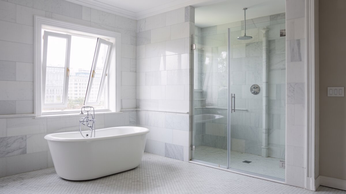 White freestanding tub by a swing window on hexagonal marble tiles
