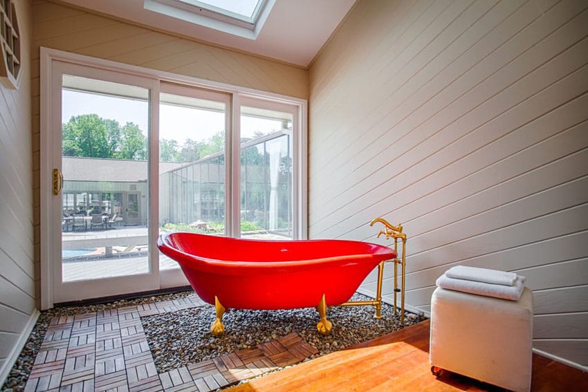 Bathroom with red acrylic claw foot bathtub and view to backyard