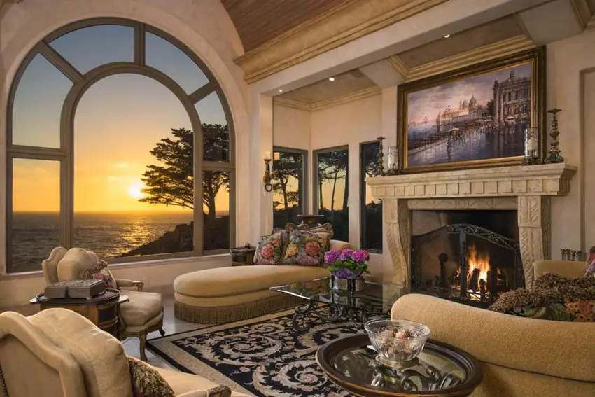 Room with large curved window, fireplace, artwork above mantel and chaise lounge