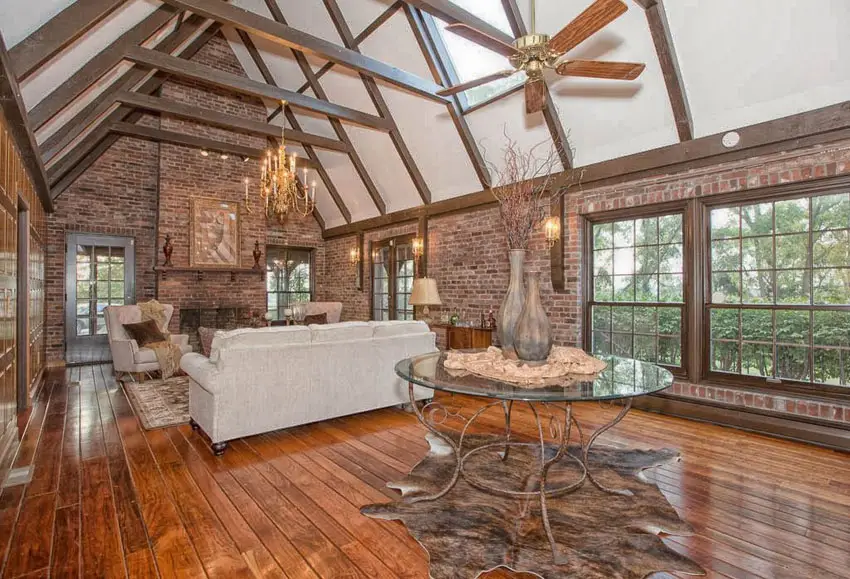 Room with high sloped ceiling, brick walls, plank floors and fireplace