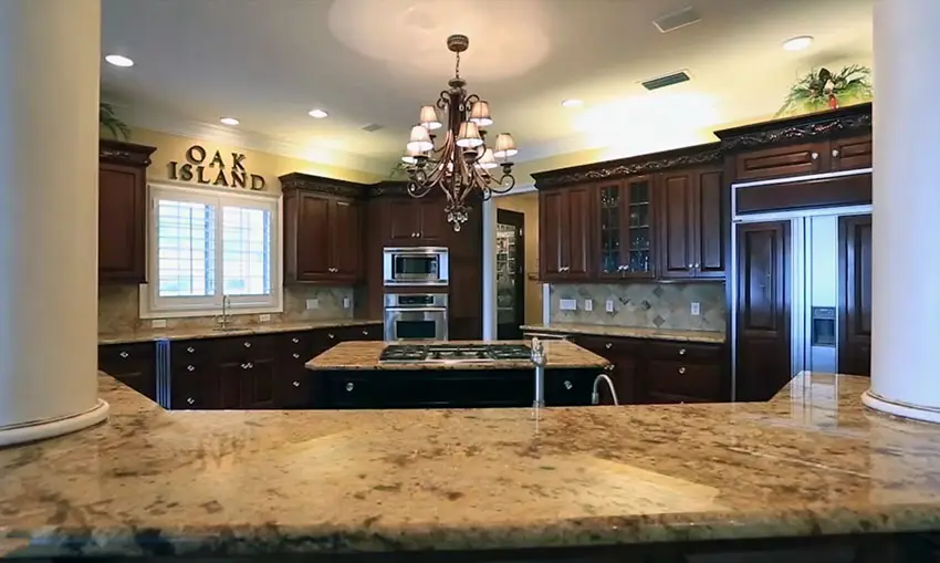 Dark wood cabinet kitchen with beige granite counters and white pillars