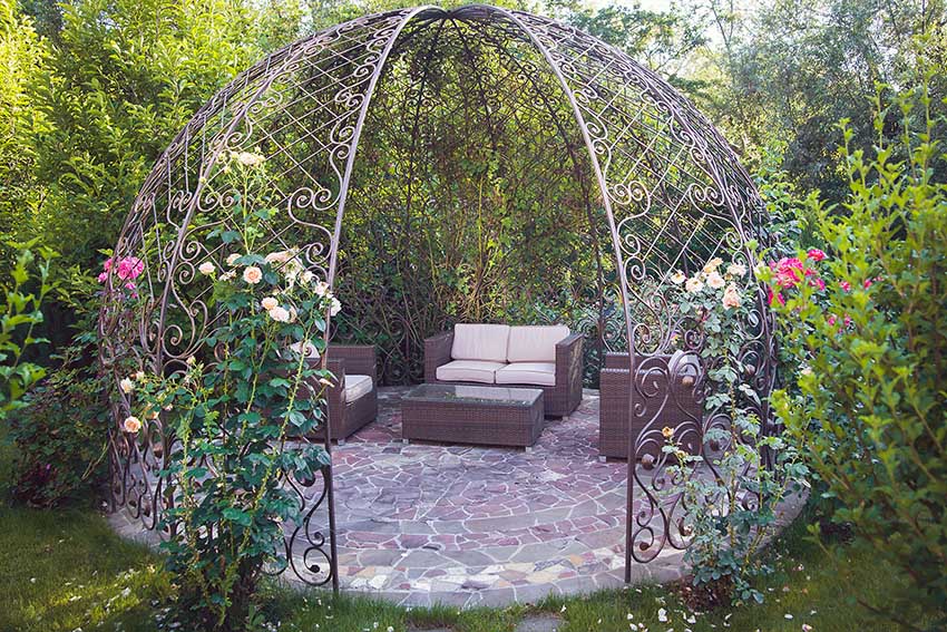 Folly gazebo in garden with metal frame outdoor furniture and rose bushes