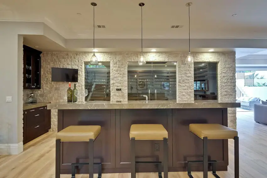 Bar with rough stacked stone walls, hanging lights and metal stools with yellow seats